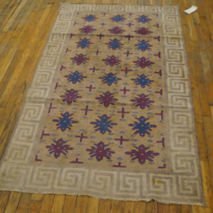 Tan field rug with blue and purple motifs and a light meander border resting on distressed wood planks.