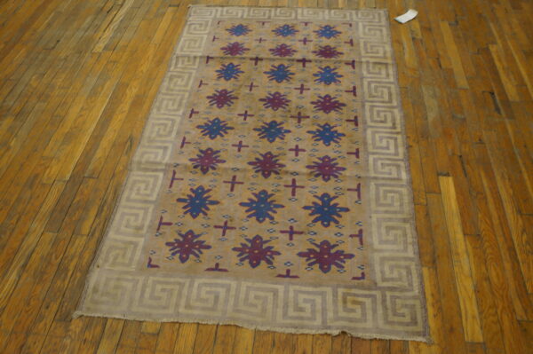Antique dhurrie small scatter size cotton brown rug 2 Tan field rug with blue and purple motifs and a light meander border resting on distressed wood planks.