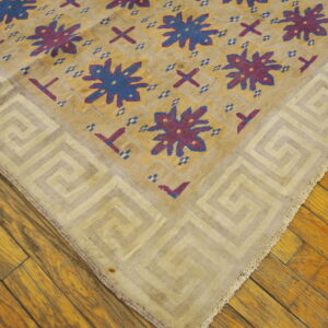 A flatwoven rug with a gold field, blue and purple stars, and a light Greek key border rests on wood floors.