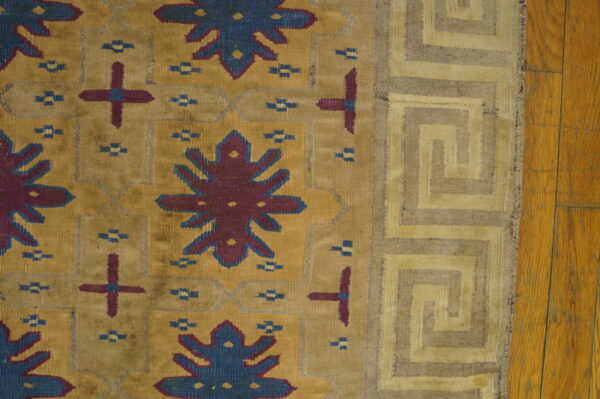 Antique dhurrie small scatter size cotton brown rug 4 Close-up of a flatweave rug with mustard field, blue and burgundy motifs, and a tan greek key border on wood floor.
