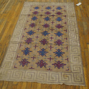 Tan rug with alternating blue and burgundy star patterns and a Greek key border on a hardwood floor.