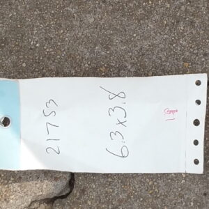 A light beige textured rug edge sits next to a handwritten tag on cracked, gray outdoor concrete.