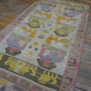 Colorful flatweave runner rug displaying stylized figures and geometric borders on distressed wood flooring.