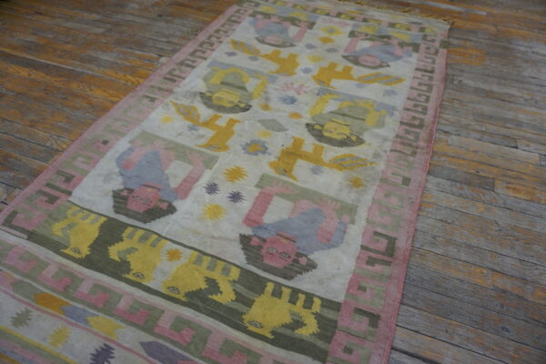 Colorful flatweave runner rug displaying stylized figures and geometric borders on distressed wood flooring.