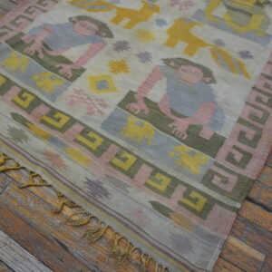 Muted pink, blue, yellow, and green flatweave rug with figures on distressed wood planks.
