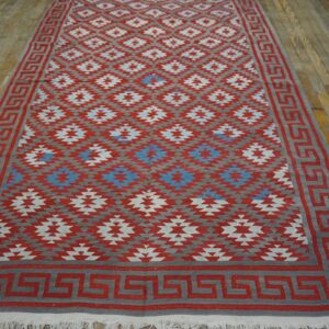 Red, gray, and blue geometric flatweave rug with a Greek key border on distressed wood flooring.