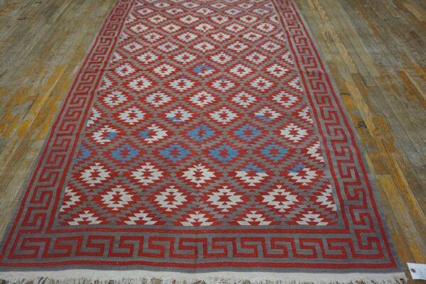 Red, gray, and blue geometric flatweave rug with a greek key border on distressed wood flooring.