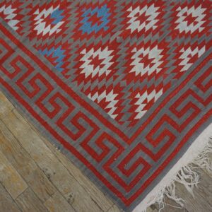 Flatwoven red, gray, and blue rug with star patterns and a Greek key border on distressed wood floor.