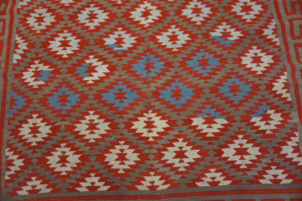 Flatweave rug featuring stepped geometric medallions in red, gray, off-white, and bright blue colors.