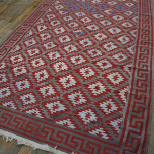 Geometric red and gray flatweave rug with a Greek key border lying on distressed wooden planks.