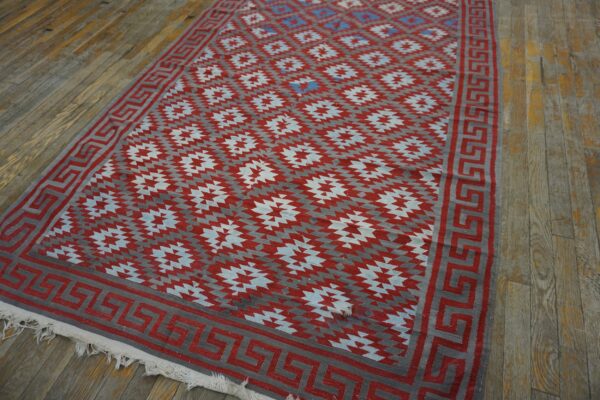 Geometric red and gray flatweave rug with a greek key border lying on distressed wooden planks.