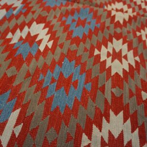 Close-up of a flatweave rug with jagged geometric designs in red, gray, blue, and white.