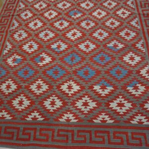 Red, gray, and blue geometric flat-weave rug with a Greek key border on distressed wood flooring.