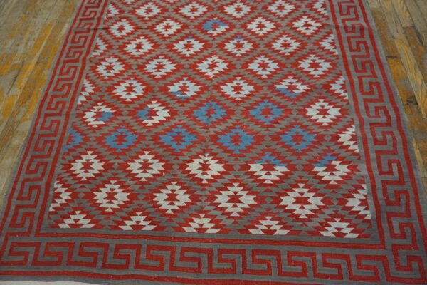 Red, gray, and blue geometric flat-weave rug with a greek key border on distressed wood flooring.