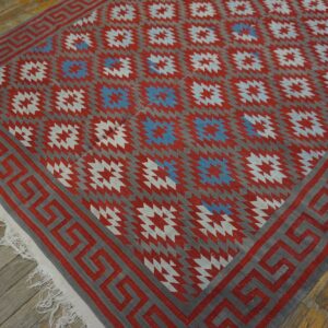 Flat-weave rug featuring red, gray, and blue geometric patterns with a Greek key border on wood floor.