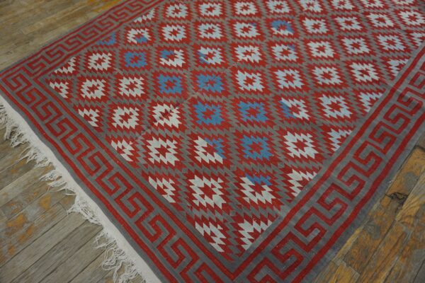 Flat-weave rug featuring red, gray, and blue geometric patterns with a greek key border on wood floor.