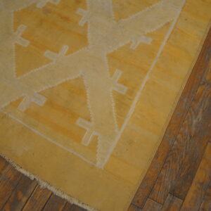 Yellow flatweave rug with light geometric patterns on rustic brown hardwood flooring.