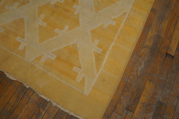 Yellow flatweave rug with light geometric patterns on rustic brown hardwood flooring.