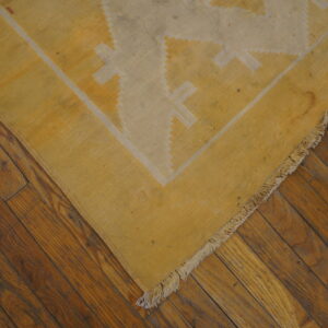 Yellow and cream flatweave rug featuring geometric patterns rests on dark hardwood flooring.