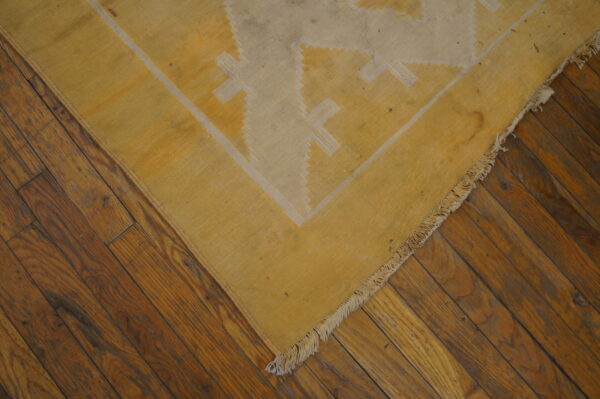 Yellow and cream flatweave rug featuring geometric patterns rests on dark hardwood flooring.