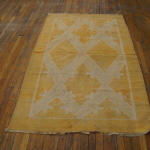 Low-profile yellow rug featuring a large white geometric zigzag pattern, resting on dark hardwood floorboards.