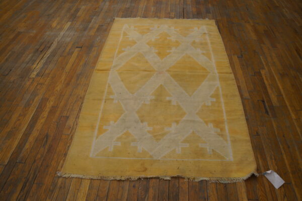 Low-profile yellow rug featuring a large white geometric zigzag pattern, resting on dark hardwood floorboards.