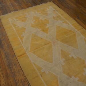 A mustard yellow flatweave rug with a cream geometric pattern lays on rustic dark wood flooring.