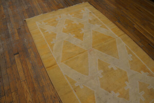A mustard yellow flatweave rug with a cream geometric pattern lays on rustic dark wood flooring.