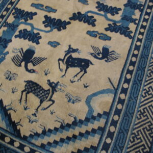 Beige rug with deep blue figures of deer, birds, and trees, framed by detailed geometric borders.