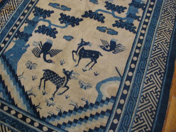 Beige rug with deep blue figures of deer, birds, and trees, framed by detailed geometric borders.