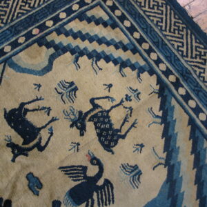 Beige rug featuring dark blue animal figures, elaborate geometric borders, and set on wood plank flooring.
