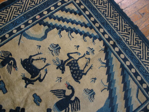 Beige rug featuring dark blue animal figures, elaborate geometric borders, and set on wood plank flooring.