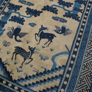 Cream rug with blue animal, tree, and cloud motifs bordered by complex geometric patterns.