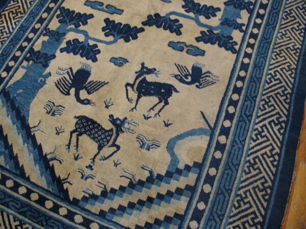 Cream rug with blue animal, tree, and cloud motifs bordered by complex geometric patterns.