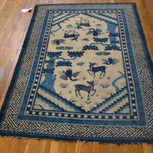 Navy and beige rug with animal motifs and geometric borders lies on glossy hardwood flooring.