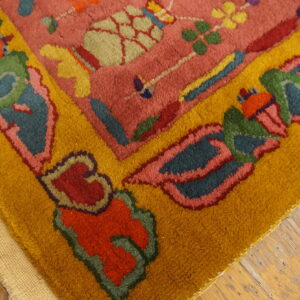 Detail view of a rose rug with colorful floral motifs and a thick golden yellow border on worn wood planks.