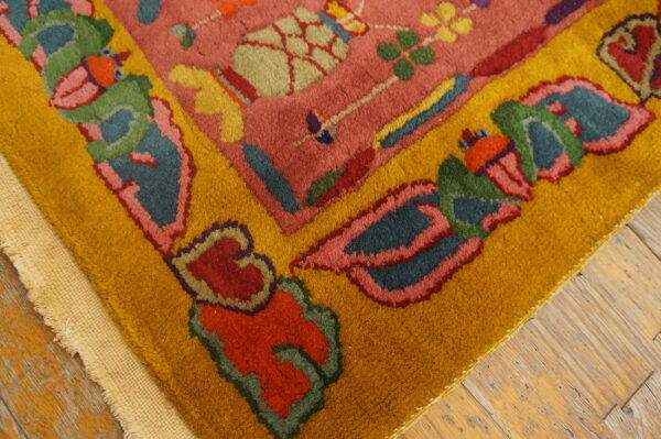 Detail view of a rose rug with colorful floral motifs and a thick golden yellow border on worn wood planks.