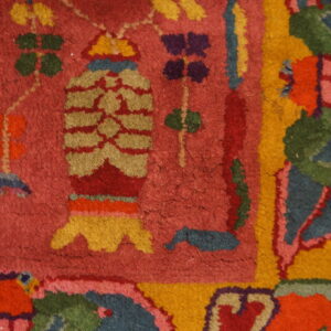Close-up of a rug showing bright stylized patterns in red, yellow, green, blue, and purple on a magenta field.