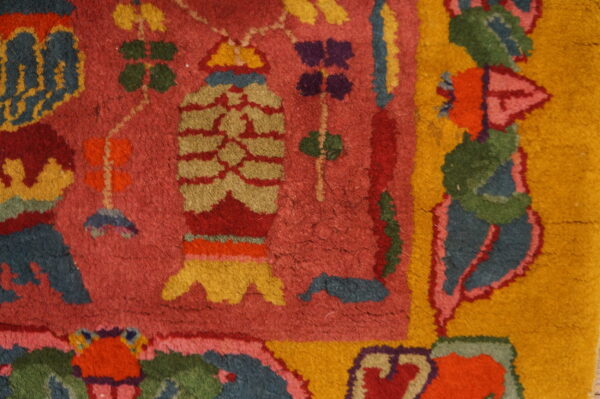Close-up of a rug showing bright stylized patterns in red, yellow, green, blue, and purple on a magenta field.