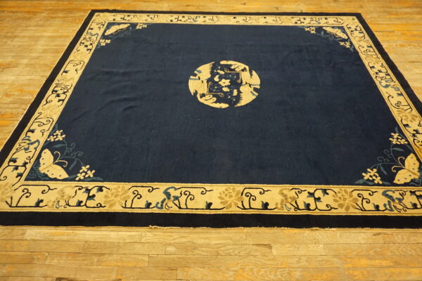 Navy rug with beige borders and a central circular bird design rests on wide-plank wood flooring.
