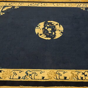 Dark blue rug with beige bird medallion and butterfly corners rests on light hardwood floors.