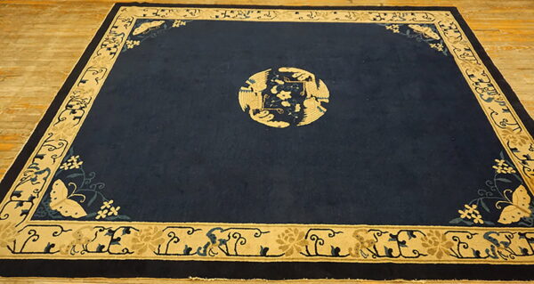 Dark blue rug with beige bird medallion and butterfly corners rests on light hardwood floors.