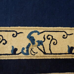 High-pile rug border in navy blue and tan featuring stylized floral scrolls and lighter blue accents.