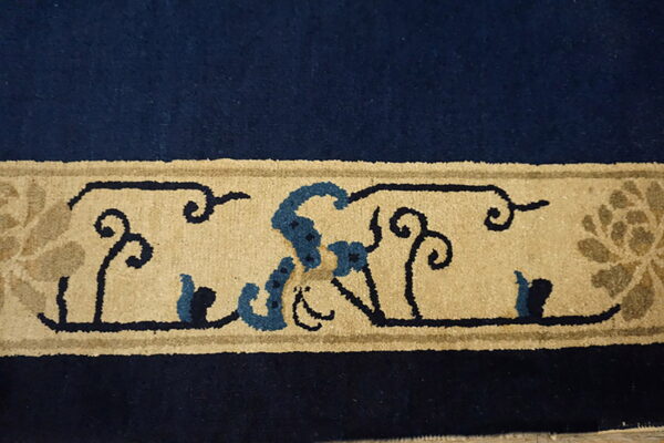 High-pile rug border in navy blue and tan featuring stylized floral scrolls and lighter blue accents.