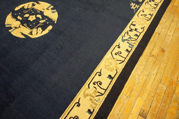 Navy blue rug featuring a vibrant yellow stylized medallion and border on worn hardwood floors.
