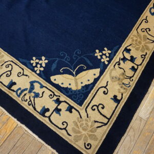 Corner detail of a deep blue rug with a beige floral and butterfly border on weathered hardwood flooring.
