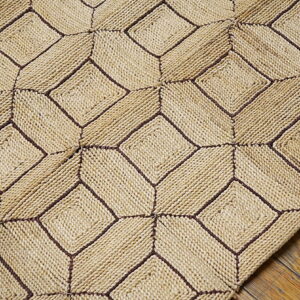 Textured beige rug featuring dark stitching in a geometric tumbling block pattern over rustic hardwood flooring.