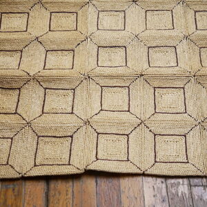 Chunky woven rug with a beige and dark brown geometric square pattern covers a wood plank floor.