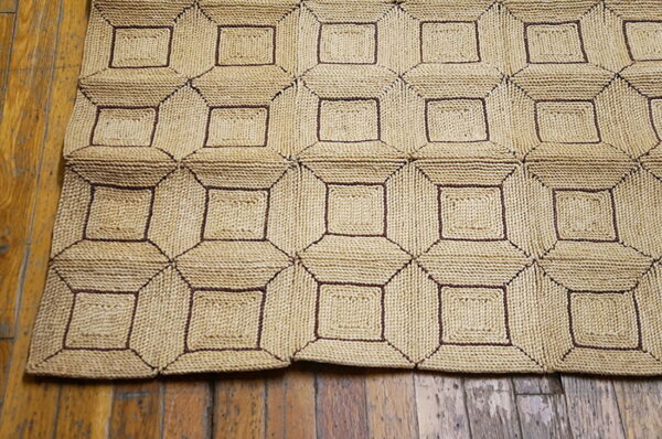 Chunky woven rug with a beige and dark brown geometric square pattern covers a wood plank floor.