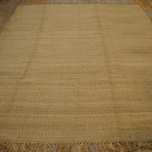Tan, textured flatweave rug with fringe displayed on rustic light brown wooden floor planks.
